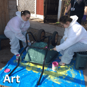 two students painting a wheelbarrow bright colours